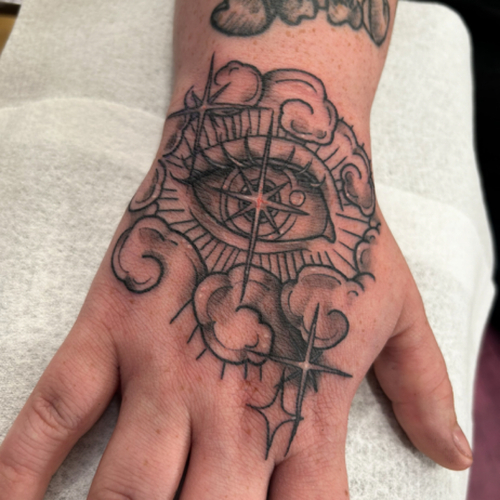A Neo Traditional eye tattoo with clouds on the hand, blending classic and modern elements. This design features a striking eye surrounded by soft, swirling clouds, creating a mysterious and captivating piece.